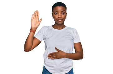 Young african american woman wearing casual white t shirt swearing with hand on chest and open...