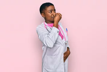 Foto op Canvas Young african american woman wearing doctor uniform and stethoscope smelling something stinky and disgusting, intolerable smell, holding breath with fingers on nose. bad smell © Krakenimages.com