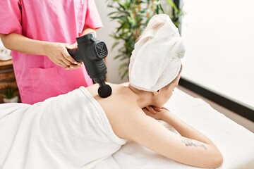 Woman reciving back massage using gun percusion at beauty center.