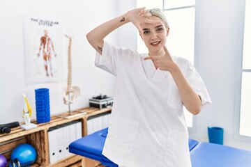 Young caucasian woman working at pain recovery clinic smiling making frame with hands and fingers with happy face. creativity and photography concept.