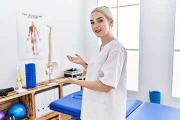 Young caucasian woman working at pain recovery clinic inviting to enter smiling natural with open hand