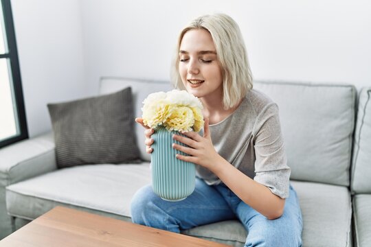 Young Caucasian Woman Smiling Confident Smelling Flowers At Home