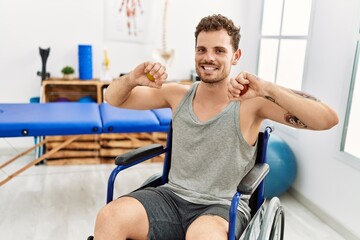Young hispanic man doing rehab using anti stress ball sitting on wheelchair at clinic