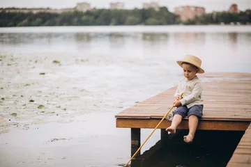 Foto op Canvas Little boy is fishing on the pier wearing a hat and a fishing rod in his hands © Viktoriia