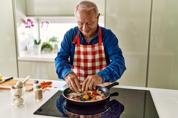 Senior man smiling confident pouring egg on frying pan at kitchen