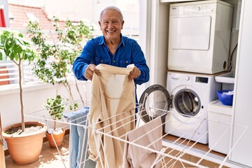 Senior caucasian man smiling happy putting clothes on clothesline at the terrace.
