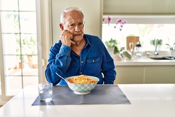 Senior man with grey hair eating pasta spaghetti at home looking stressed and nervous with hands on mouth biting nails. anxiety problem.