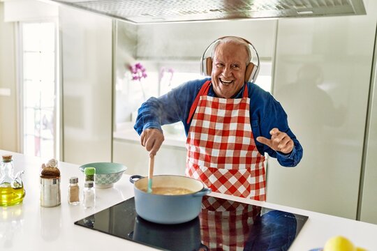 Senior man listening to music cooking spaghetti at kitchen