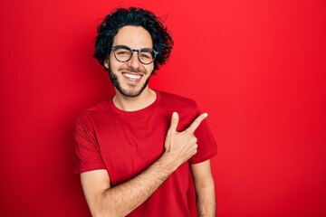 Handsome hispanic man wearing casual t shirt and glasses cheerful with a smile of face pointing...
