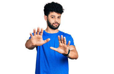 Young arab man with beard wearing casual blue t shirt moving away hands palms showing refusal and...