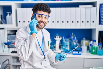Young arab man wearing scientist uniform talking on the smartphone at laboratory