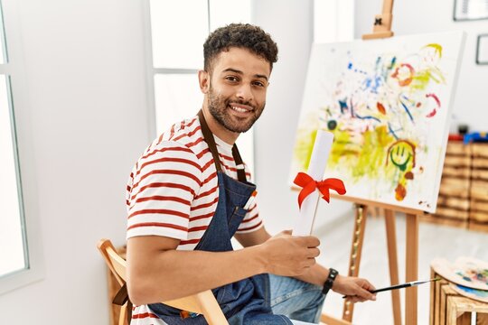 Young arab artist man smiling happy holding diploma at art studio.