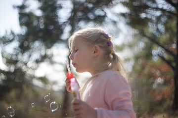 Young happy girl playing in nature with bubble blower