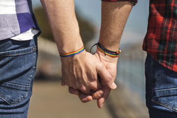 intertwined hands of gay couple with a rainbow bracelet
