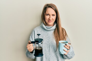 Young blonde woman drinking a cup of italian coffee skeptic and nervous, frowning upset because of problem. negative person.