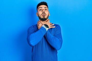 Young hispanic man with beard wearing casual blue sweater shouting suffocate because painful strangle. health problem. asphyxiate and suicide concept.