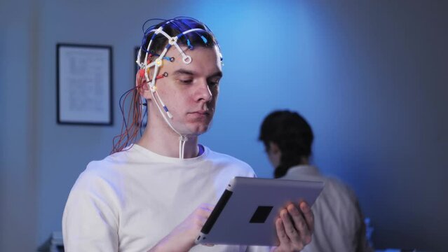 Man wearing EEG topographer for examining brain, doctor making electrogram of scalp activity. Researching of brain work using electroencephalography headset.