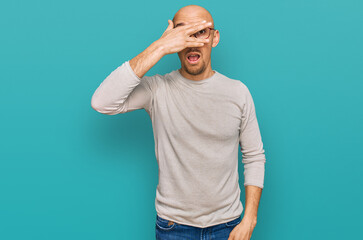 Fototapeta premium Bald man with beard wearing casual clothes and glasses peeking in shock covering face and eyes with hand, looking through fingers with embarrassed expression.