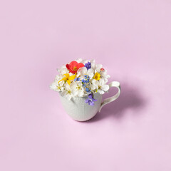 Colorful spring flowers in white cup on pastel light blue background. Creative flowers concept. Minimalistic nature composition with copy space. Spring tea idea.