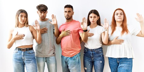 Group of young friends standing together over isolated background swearing with hand on chest and open palm, making a loyalty promise oath