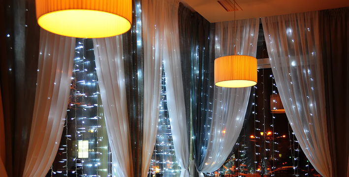 View of the evening windows decorated with garlands and lights behind the foundation of the night city.