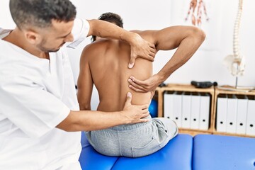 Two hispanic men physiotherapist and patient having rehab session massaging back at clinic