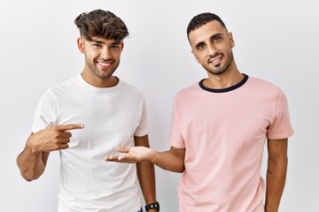 Young gay couple standing over isolated background amazed and smiling to the camera while presenting with hand and pointing with finger.