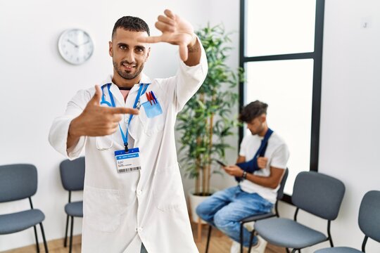 Hispanic doctor man at waiting room with pacient with arm injury smiling making frame with hands and fingers with happy face. creativity and photography concept.