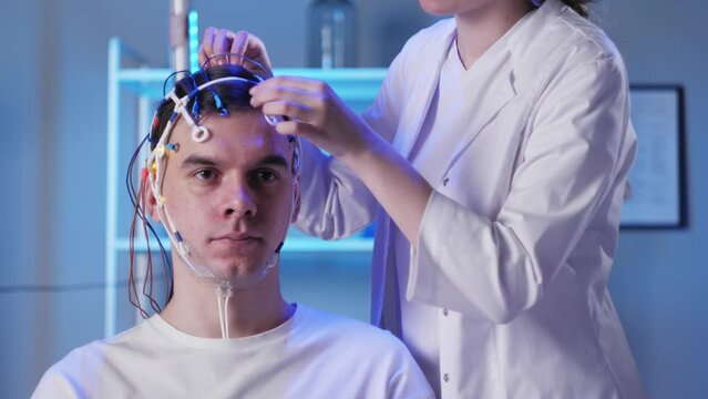Man wearing EEG topographer for examining brain, doctor making electrogram of scalp activity. Researching of brain work using electroencephalography headset.