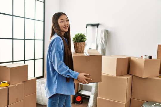 Young chinese girl smiling happy holding cardboard box at new home