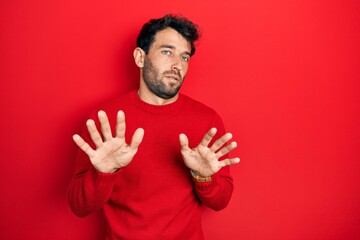 Handsome man with beard wearing casual red sweater moving away hands palms showing refusal and denial with afraid and disgusting expression. stop and forbidden.