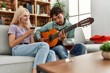 Man playing spanish guitar to his girlfriend sitting on the sofa at home.