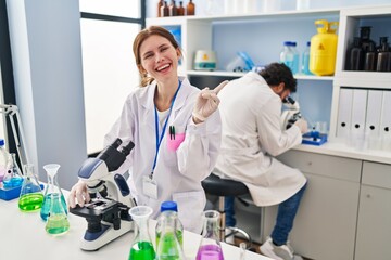 Young two people working at scientist laboratory smiling happy pointing with hand and finger to the side