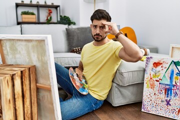 Young man with beard painting canvas at home worried and stressed about a problem with hand on...