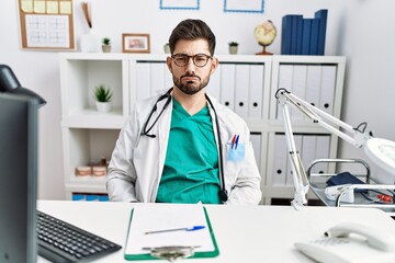 Young man with beard wearing doctor uniform and stethoscope at the clinic depressed and worry for distress, crying angry and afraid. sad expression.