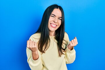 Fototapeta premium Young brunette woman wearing casual sweatshirt very happy and excited doing winner gesture with arms raised, smiling and screaming for success. celebration concept.