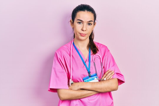 Young brunette woman wearing doctor uniform and stethoscope standing with arms crossed relaxed with serious expression on face. simple and natural looking at the camera.