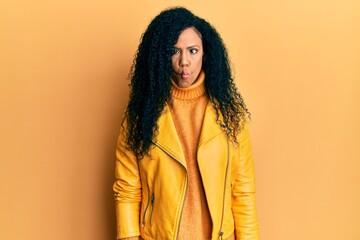Middle age african american woman wearing wool winter sweater and leather jacket making fish face with lips, crazy and comical gesture. funny expression.