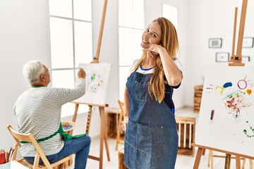 Hispanic woman wearing apron at art studio smiling doing phone gesture with hand and fingers like talking on the telephone. communicating concepts.