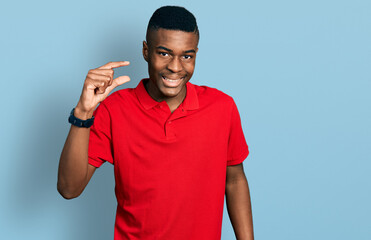 Fototapeta premium Young african american man wearing casual red t shirt smiling and confident gesturing with hand doing small size sign with fingers looking and the camera. measure concept.