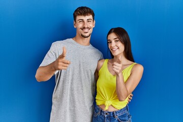 Fototapeta premium Young hispanic couple standing together over blue background pointing fingers to camera with happy and funny face. good energy and vibes.