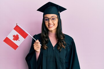 Young hispanic woman wearing graduation uniform holding canada flag looking positive and happy standing and smiling with a confident smile showing teeth