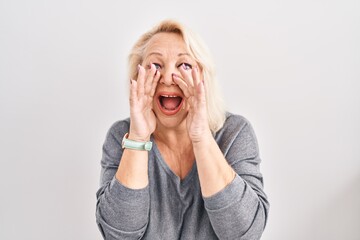 Middle age caucasian woman standing over white background shouting angry out loud with hands over mouth