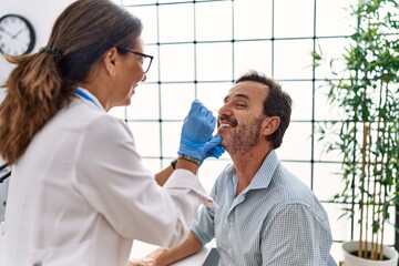 Fototapeta premium Middle age man and woman wearing doctor uniform making covid-19 test at clinic