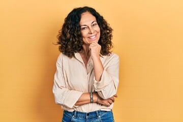 Middle age hispanic woman wearing casual clothes looking confident at the camera with smile with crossed arms and hand raised on chin. thinking positive.