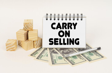 On a white surface, cubes, dollars, a pen and a notepad with the inscription - Carry on Selling