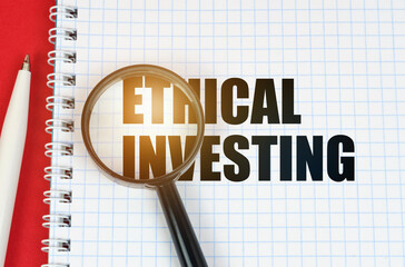 On the red surface is a pen, a notepad with the inscription - Ethical Investing and a magnifying...