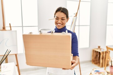 Young latin woman smiling confident opening draw briefcase at art studio