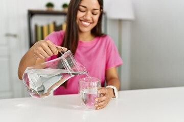 Young latin woman smiling confident pouring water at home