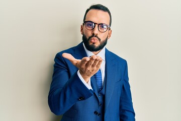 Young man with beard wearing business suit and tie looking at the camera blowing a kiss with hand on air being lovely and sexy. love expression.